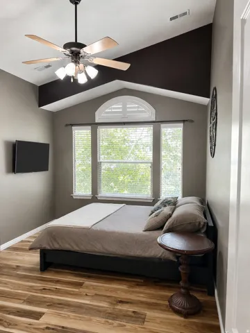 Vaulted ceiling featuring a ceiling fan with light kit, wood-finish flooring, and multiple windows with blinds and an arched transom