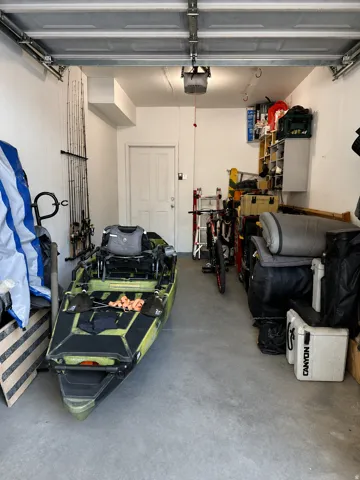 Attached  extra deep single-panel garage door with new spring and cable track system, interior access door, concrete flooring, and overhead lighting
