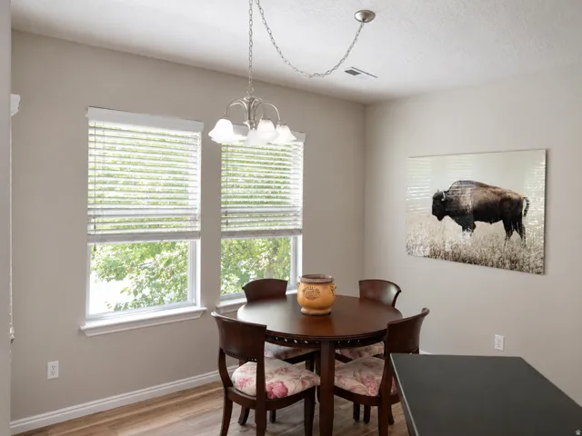 Dining area with wood-finish flooring, two large windows with blinds, and a brushed nickel chandelier