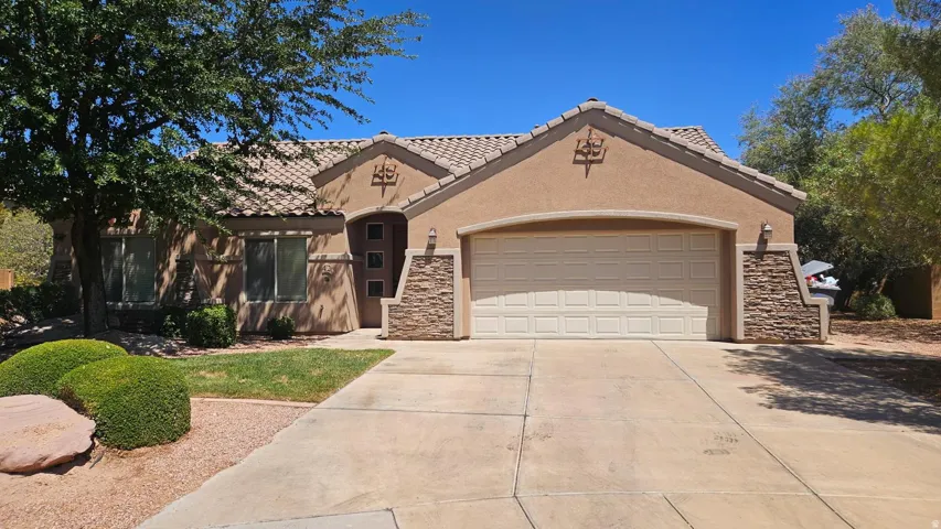 Stucco exterior with a tiled roof, integrated two-car garage, stone veneer accents, and a paved driveway