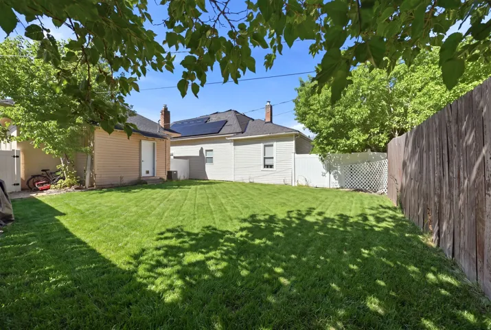Expansive lawn with established perimeter fencing, mature trees, and a detached structure featuring tan siding