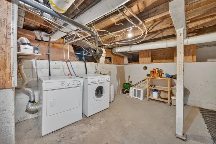 Laundry area featuring a washer and dryer unit, exposed ceiling joists, and concrete flooring