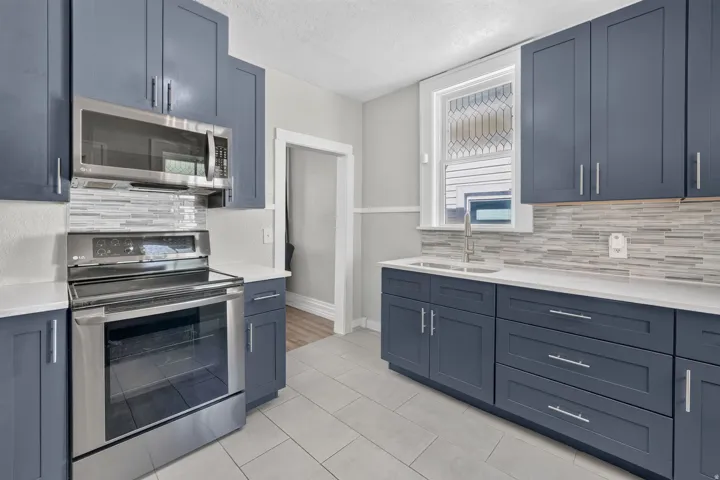 Kitchen featuring blue shaker-style cabinetry, white countertops, tile backsplash, stainless steel appliances, and tile flooring
