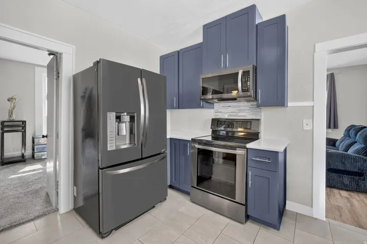 Kitchen featuring slate blue cabinetry, stainless steel appliances, white countertops, a tiled backsplash, and light-toned tile flooring
