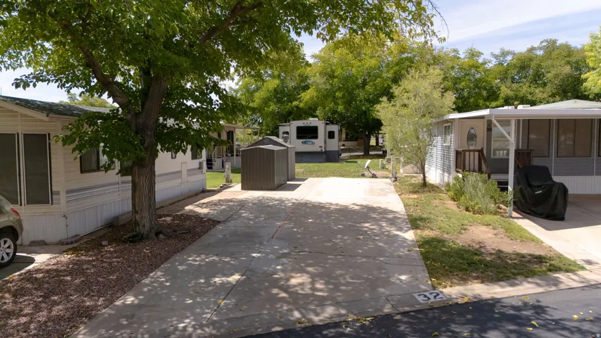 Paved driveway with designated parking, mature shade trees, gravel landscaping, and a metal storage shed