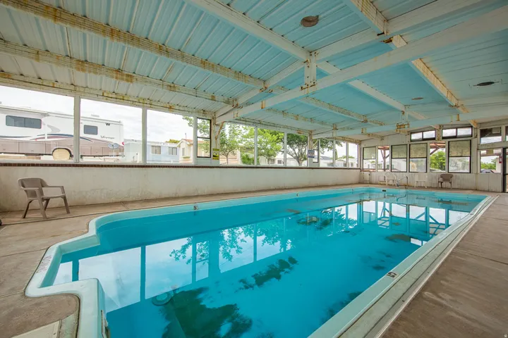 Indoor swimming pool with concrete decking, surrounded by multiple windows and a metal-paneled ceiling