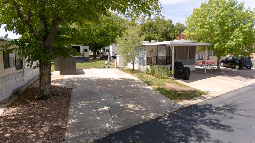 Covered outdoor patio area, attached carport, mature trees, concrete driveway, and exterior siding