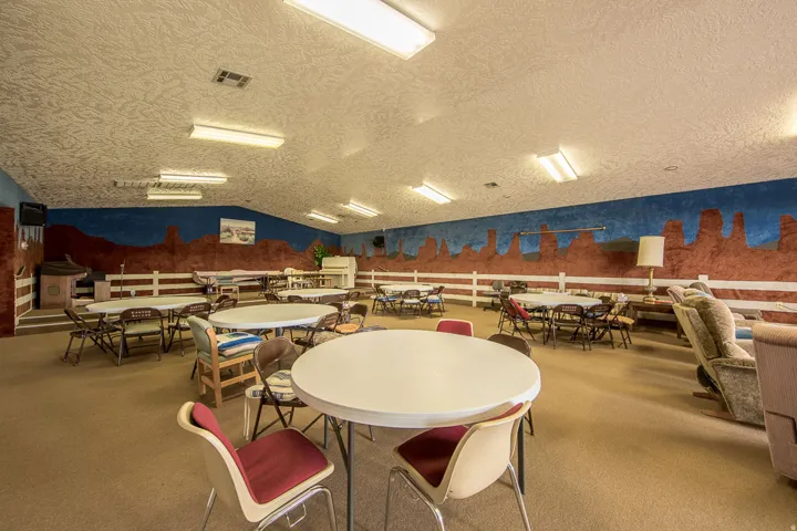 Large gathering space with textured ceiling and wall mural, featuring recessed fluorescent lighting and carpeted flooring