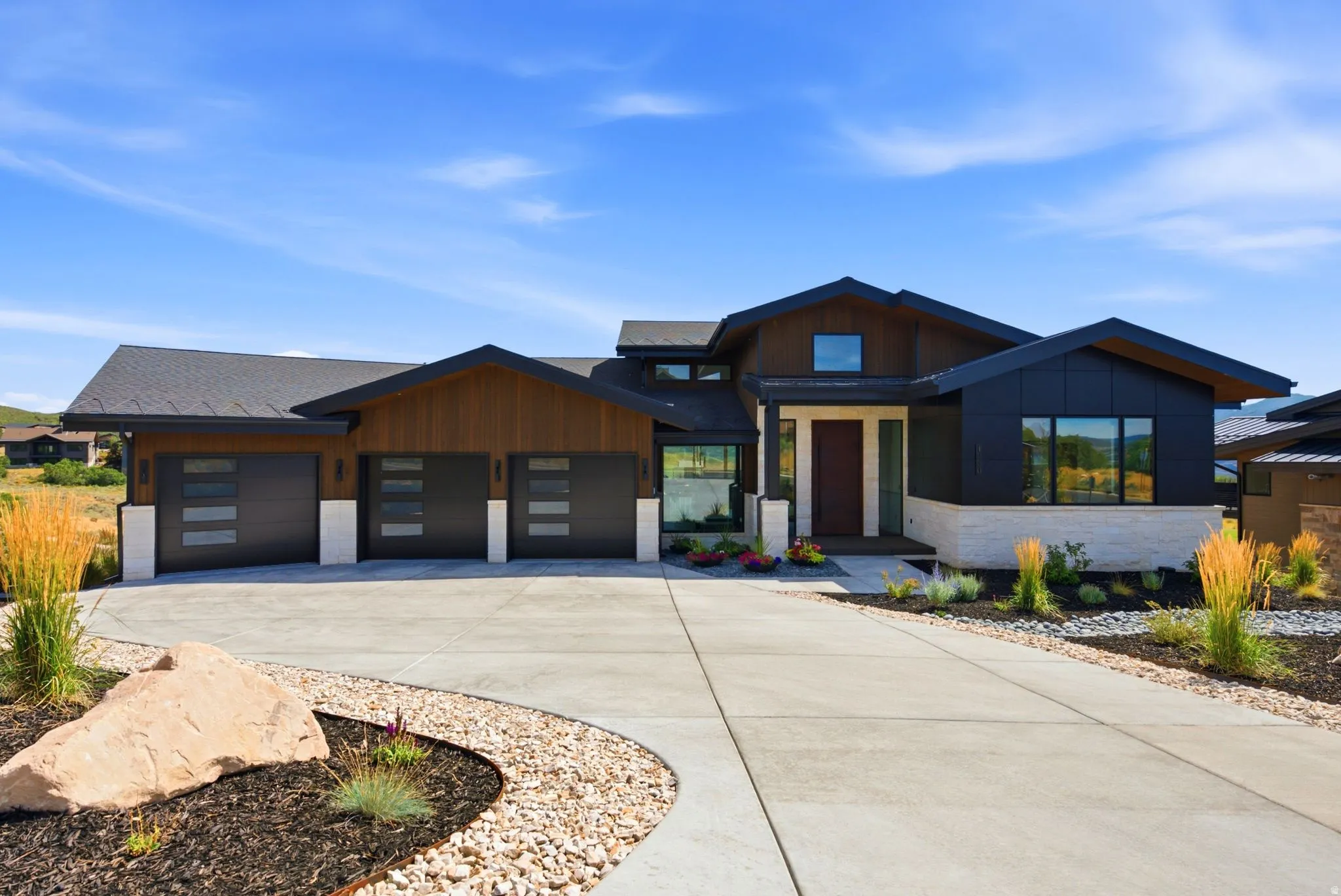 Contemporary exterior featuring wood-finish siding, dark metal accents, and a stone-clad foundation