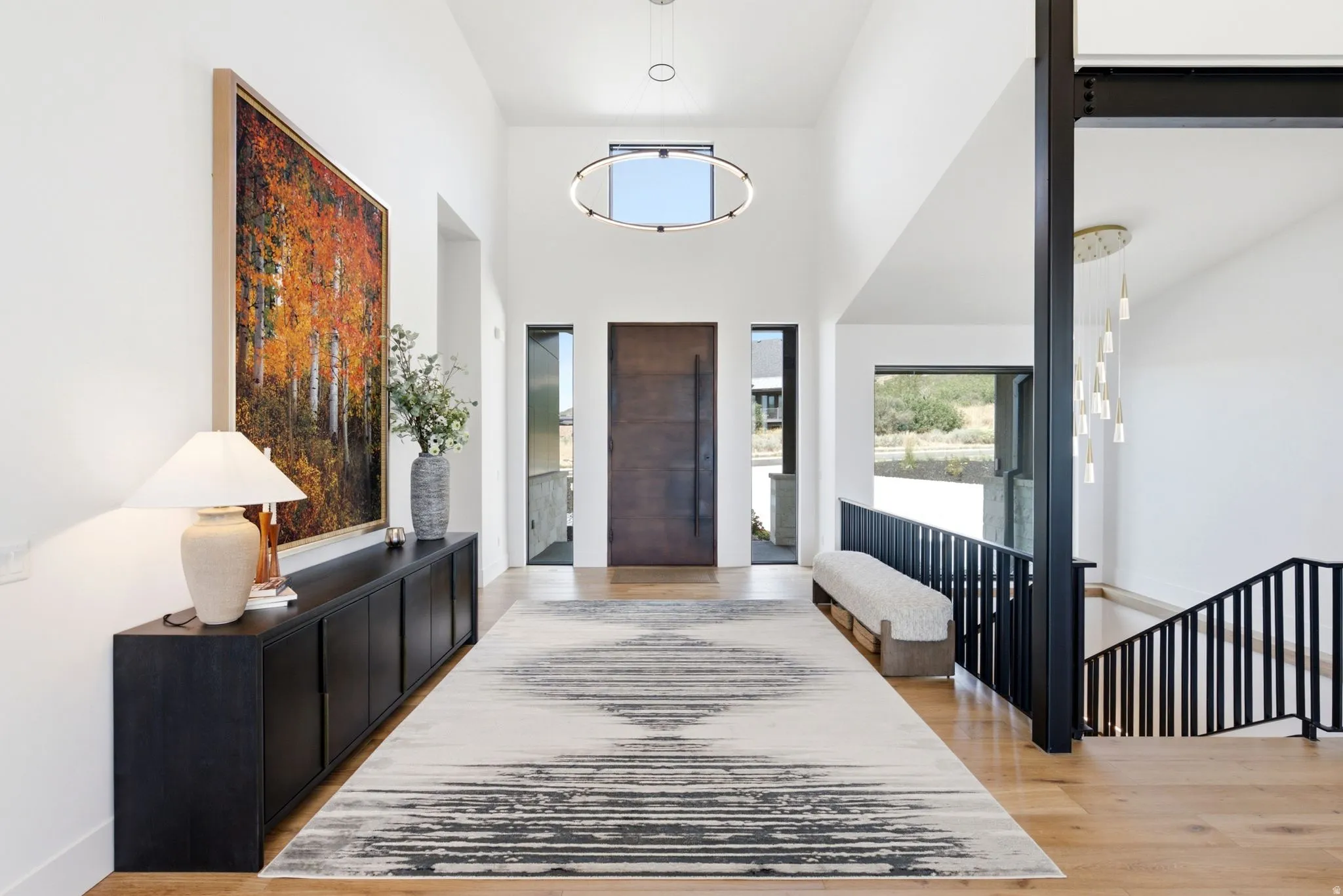 Vaulted ceilings, wood-finish flooring, a modern entry door with sidelights, and a contemporary stair railing