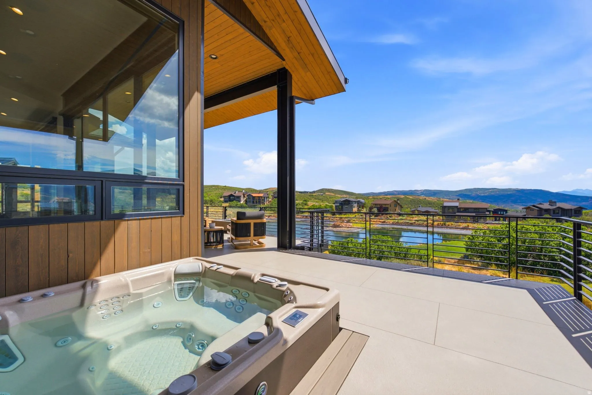 Expansive outdoor deck featuring an integrated hot tub, a contemporary cable railing system, a wood-paneled exterior, and large picture windows