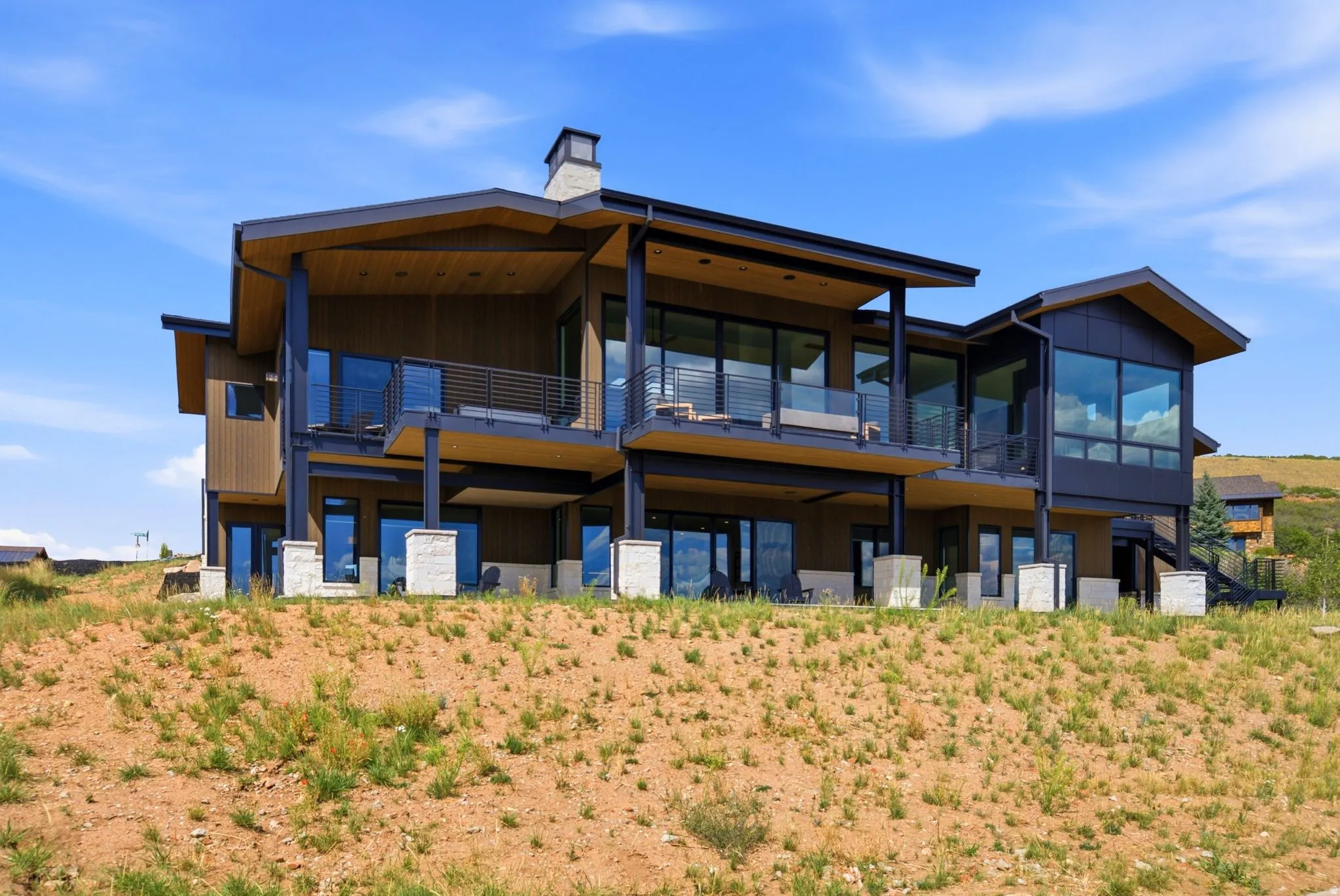 Contemporary exterior featuring expansive glazing, multiple covered balconies, a stone-clad chimney, and a multi-level design