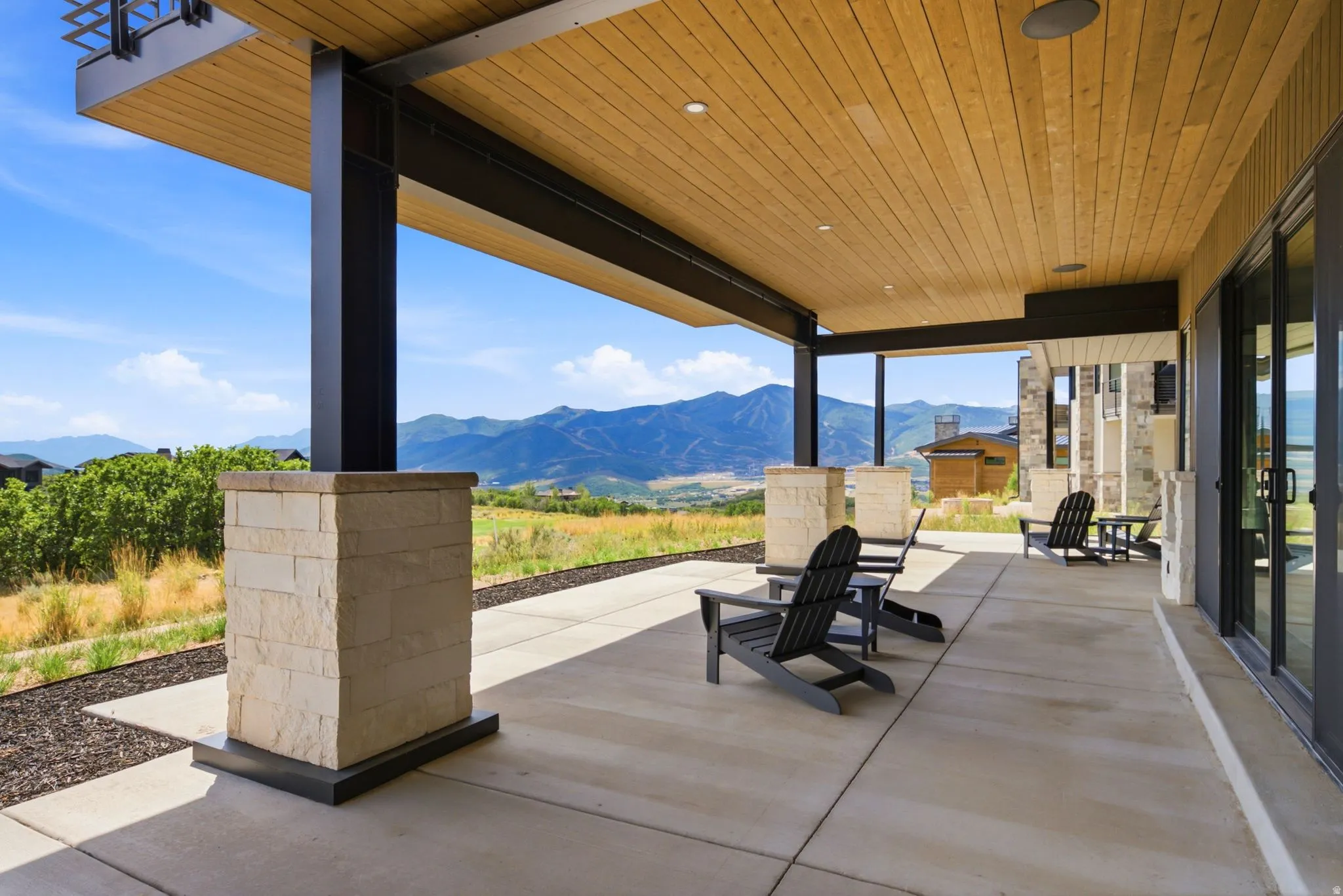 Expansive covered patio featuring a wood-finish ceiling, mountain scenery, concrete flooring, and stone-clad pillars