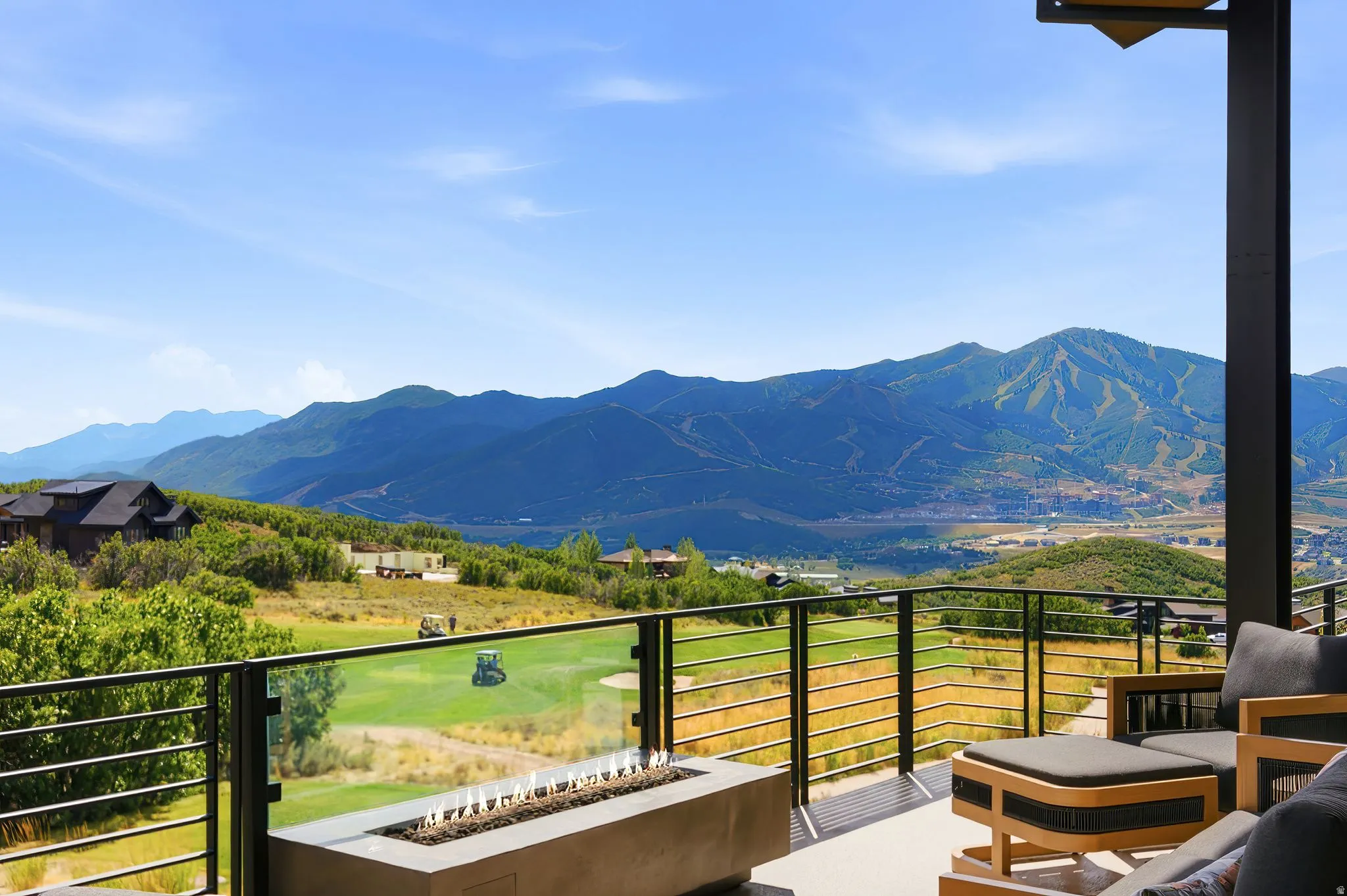 Expansive outdoor terrace featuring a built-in fire pit, glass and metal railing, and a mountain and golf course backdrop
