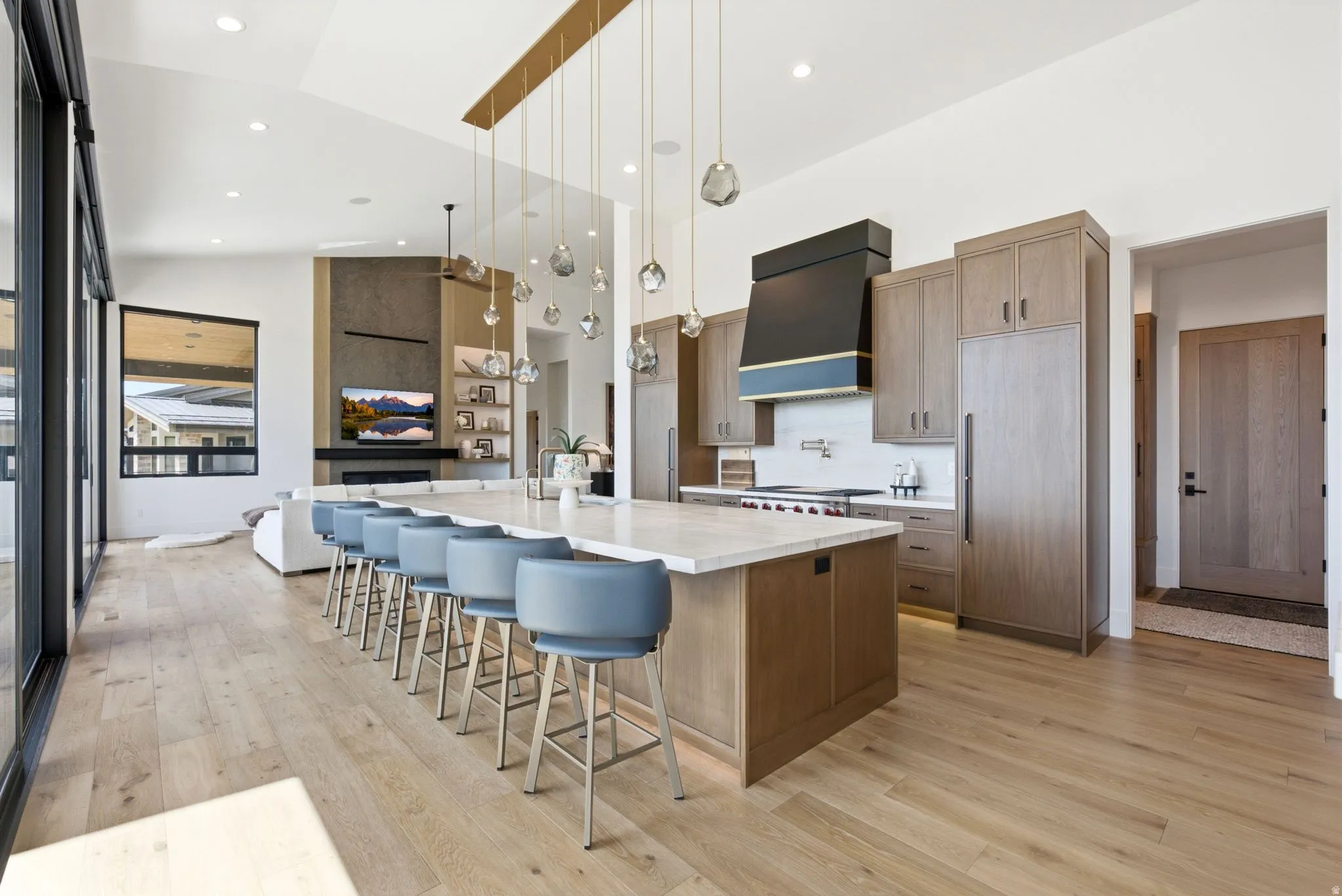 Open-concept living space with vaulted ceilings, large sliding glass doors, a kitchen island with seating, built-in appliances, and light wood-finish flooring