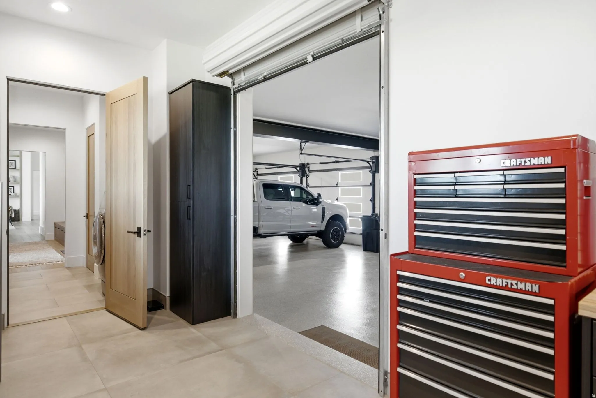 Oversized garage entry with a rolling overhead door, large format tile flooring, and integrated dark wood-finish cabinetry