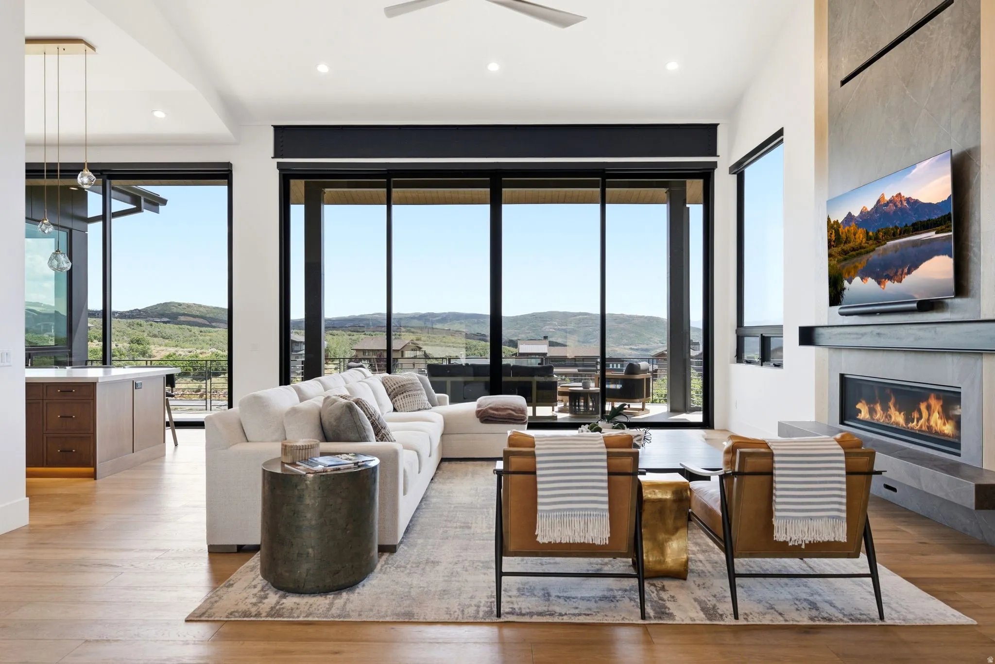 Expansive sliding glass doors, built-in linear fireplace, recessed lighting, wood-finish flooring, and a ceiling fan