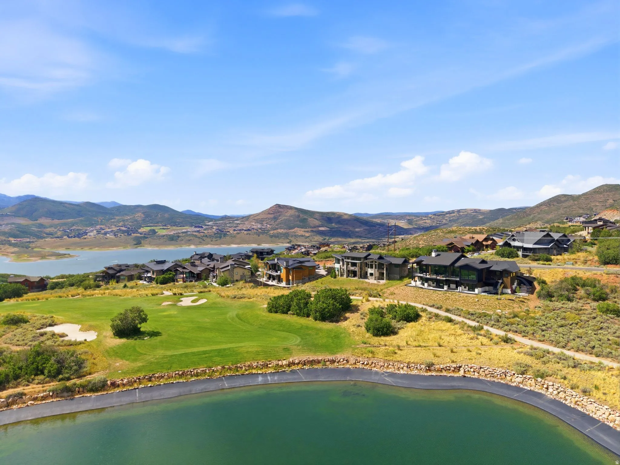 Expansive hillside property featuring a manicured golf course, a large water feature, and distant mountain and lake scenery