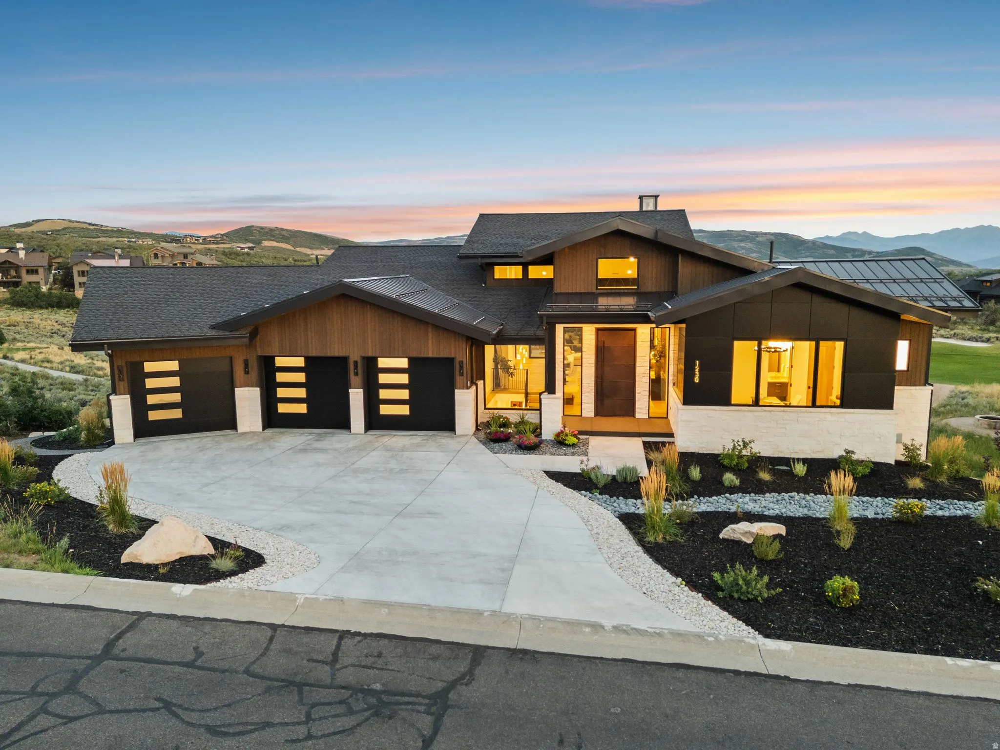Contemporary exterior with wood siding accents, a multi-car garage with modern doors, a concrete driveway, and structured landscaping featuring decorative rock