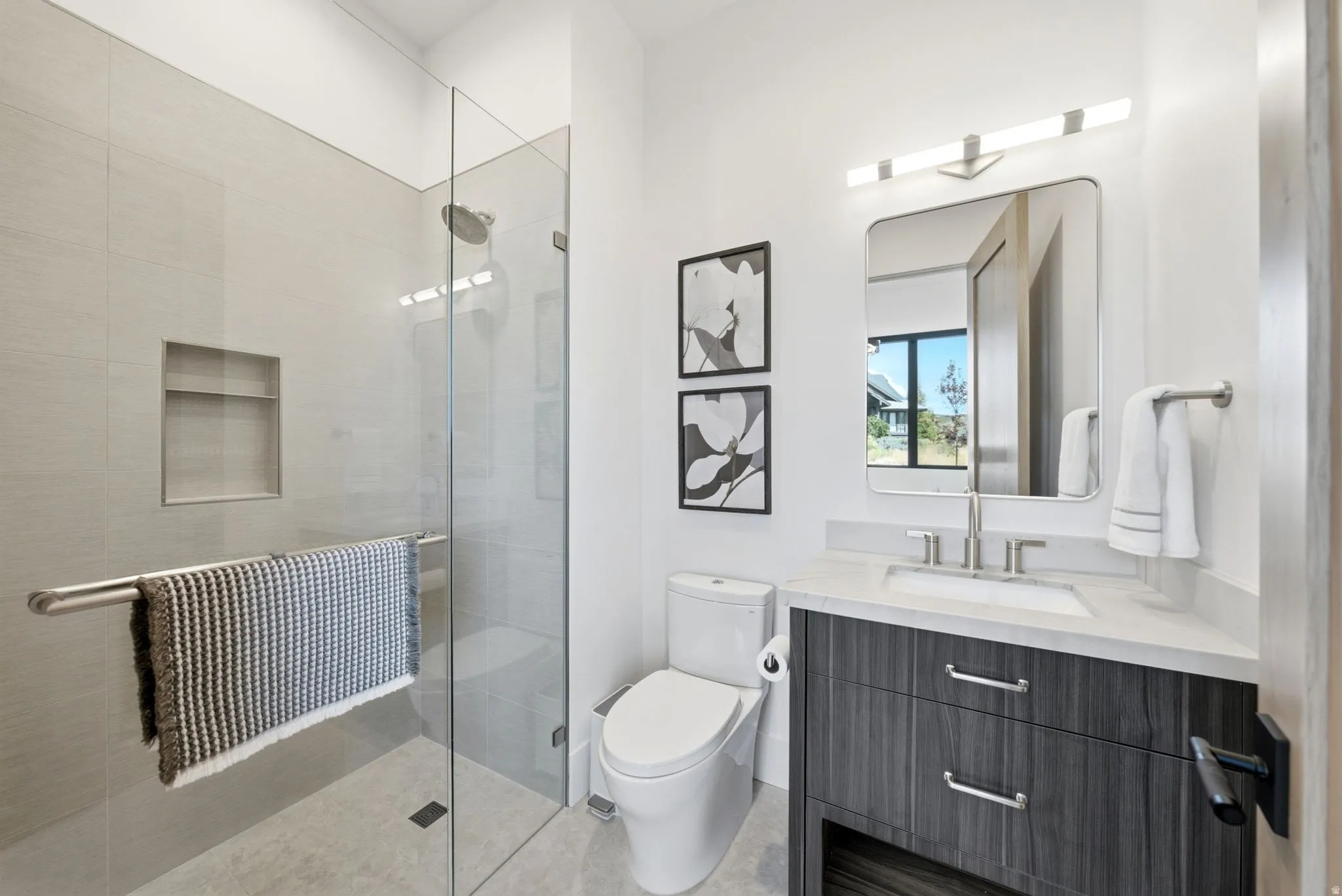 Glass-enclosed shower with a recessed niche, rainfall showerhead, and tiled flooring
