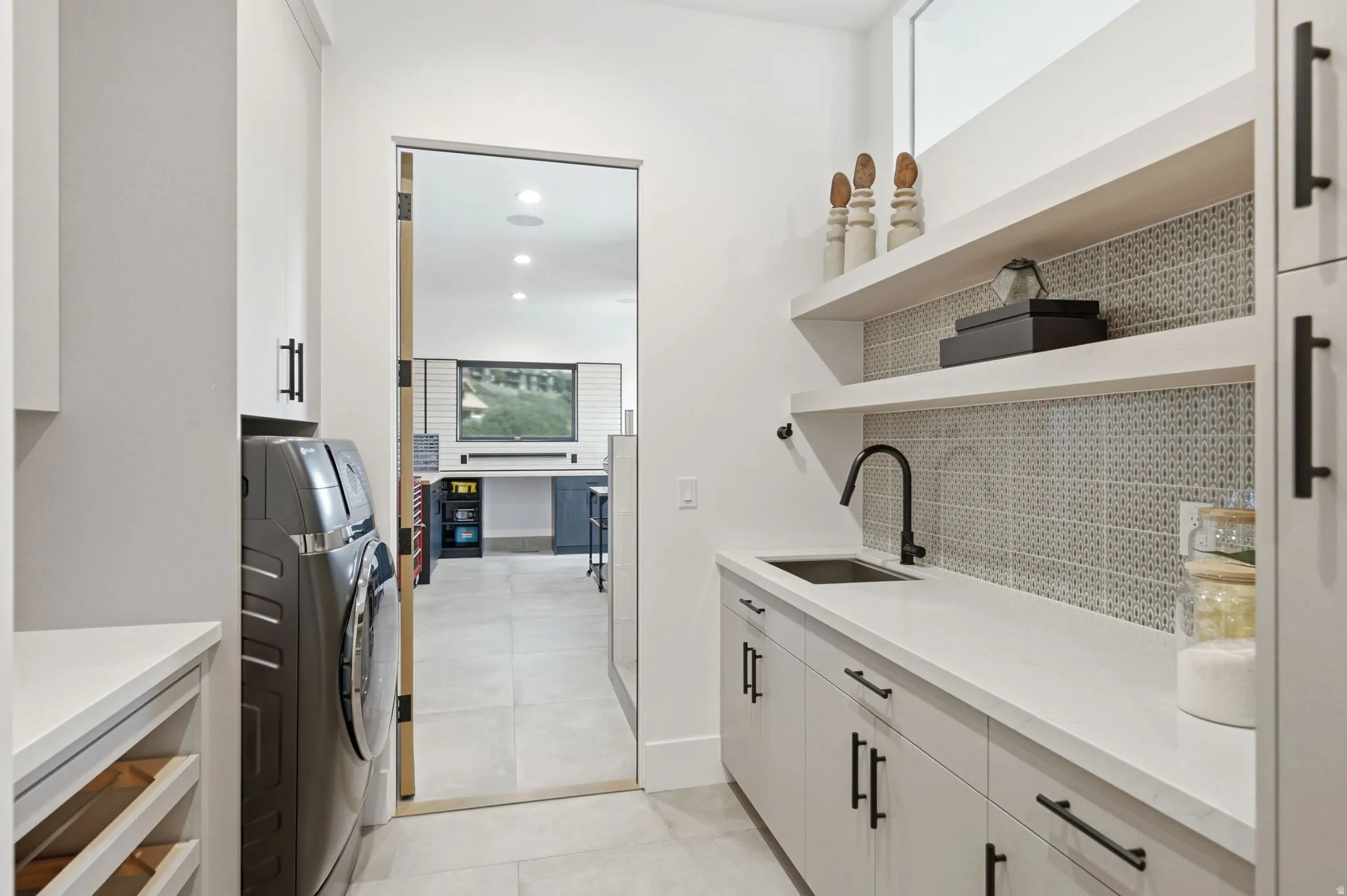 Laundry area featuring built-in cabinetry, an integrated sink with a matte black faucet, open shelving, and a tiled backsplash