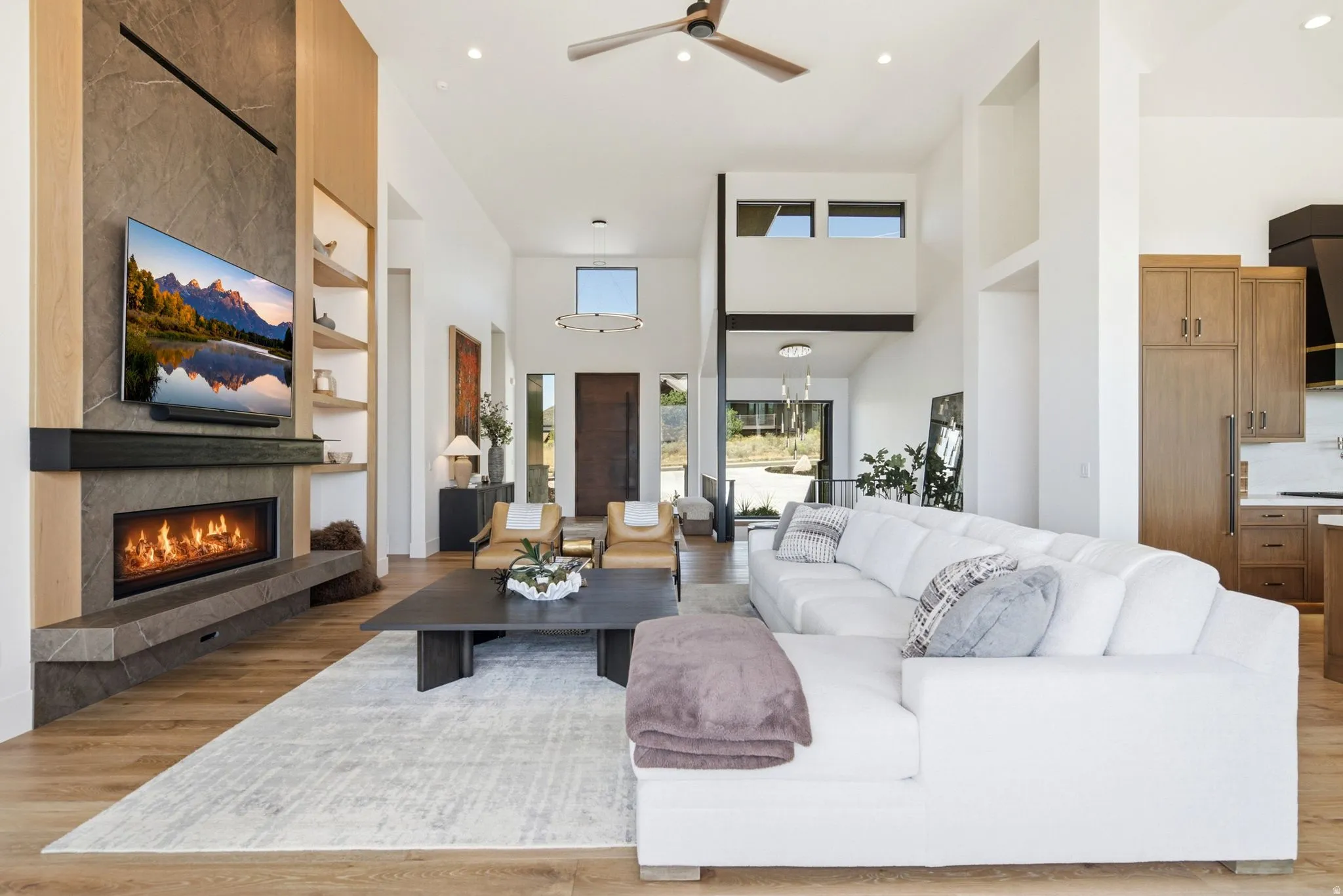 Two-story living area featuring wood-finish flooring, a contemporary fireplace with a stone surround, and integrated shelving