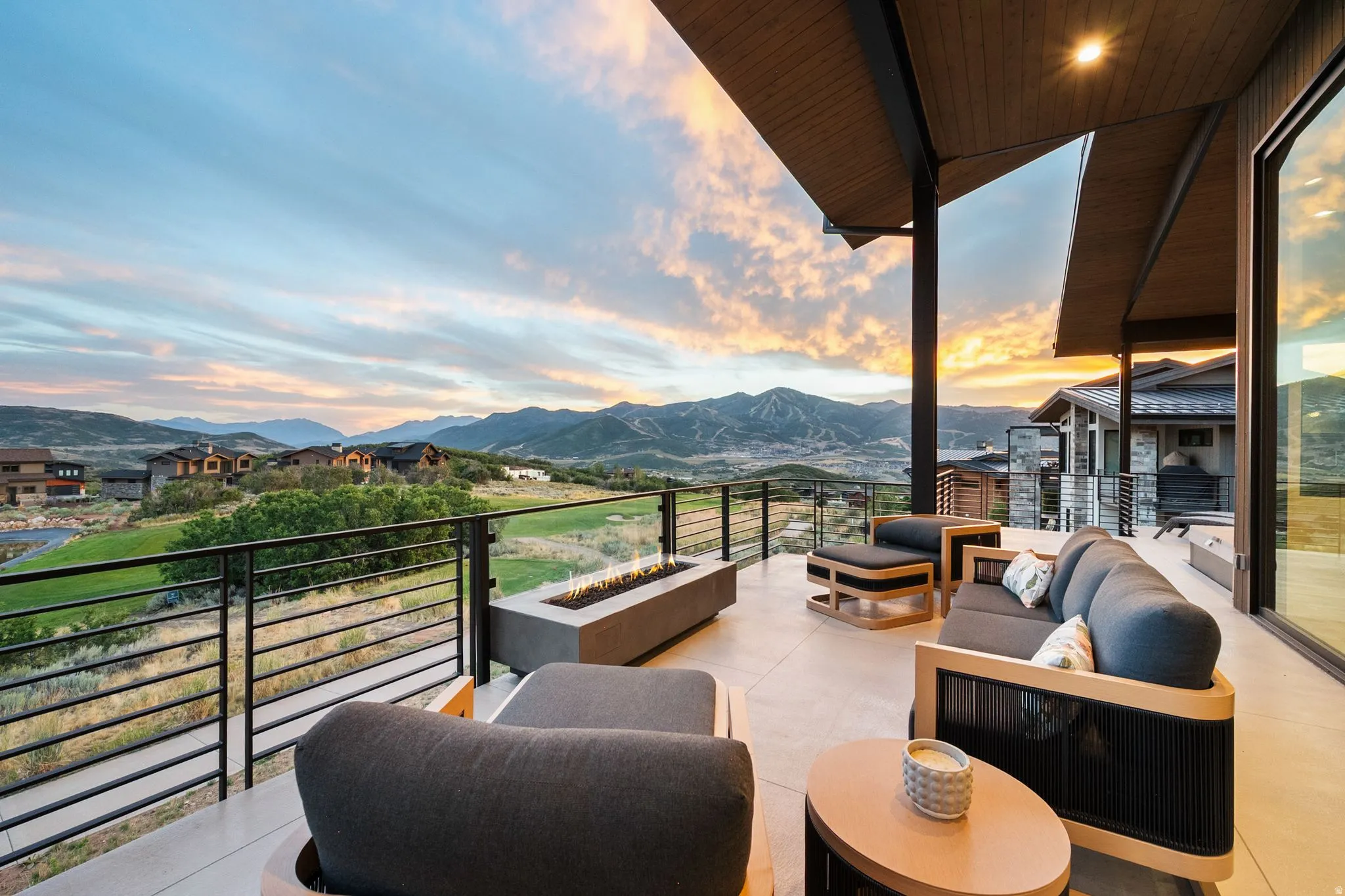 Expansive outdoor terrace featuring a built-in linear fire pit, metal and glass railing, and a tongue-and-groove wood ceiling