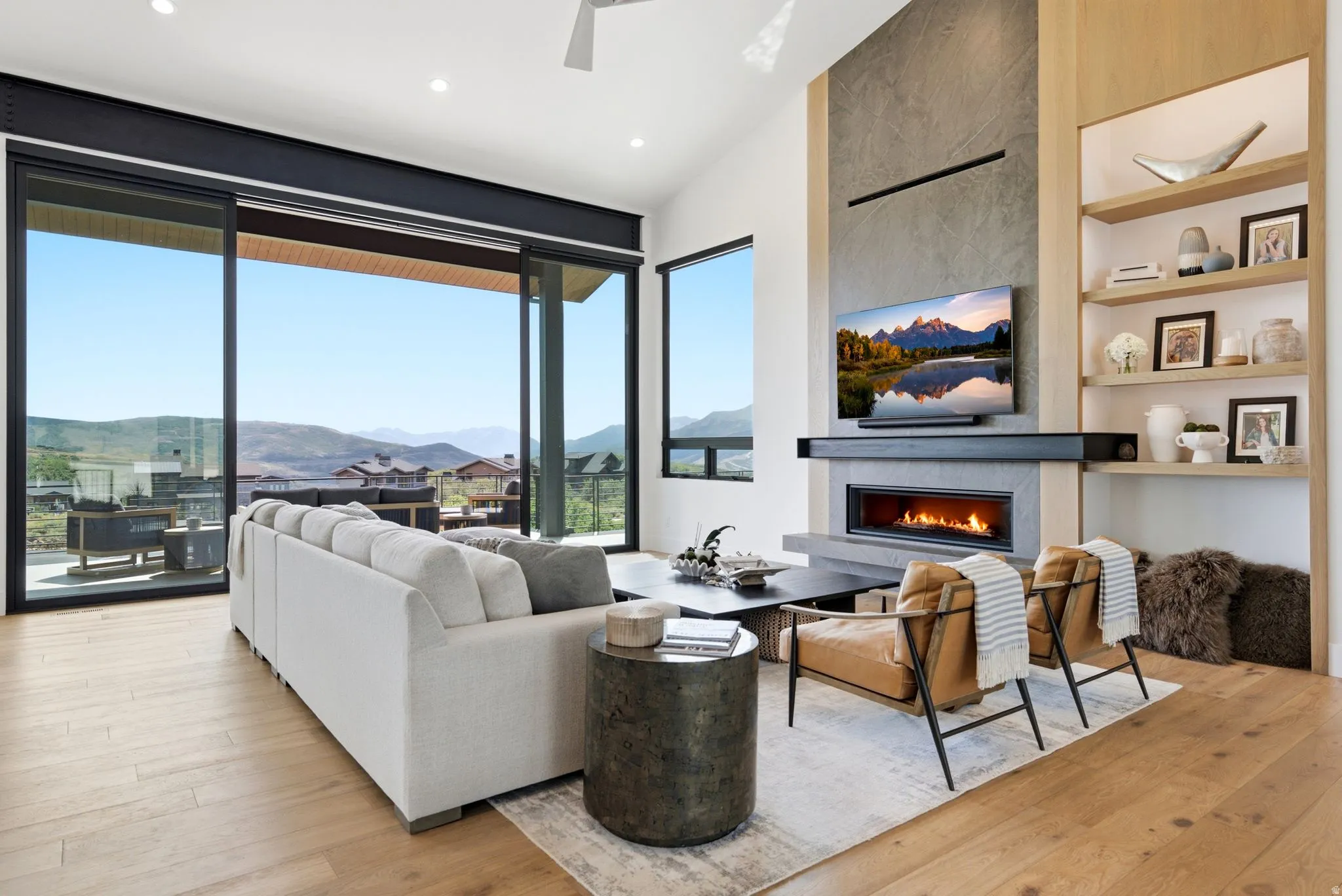 Spacious living area featuring large sliding glass doors, a linear fireplace with a stone surround, built-in shelving, and wood-finish flooring