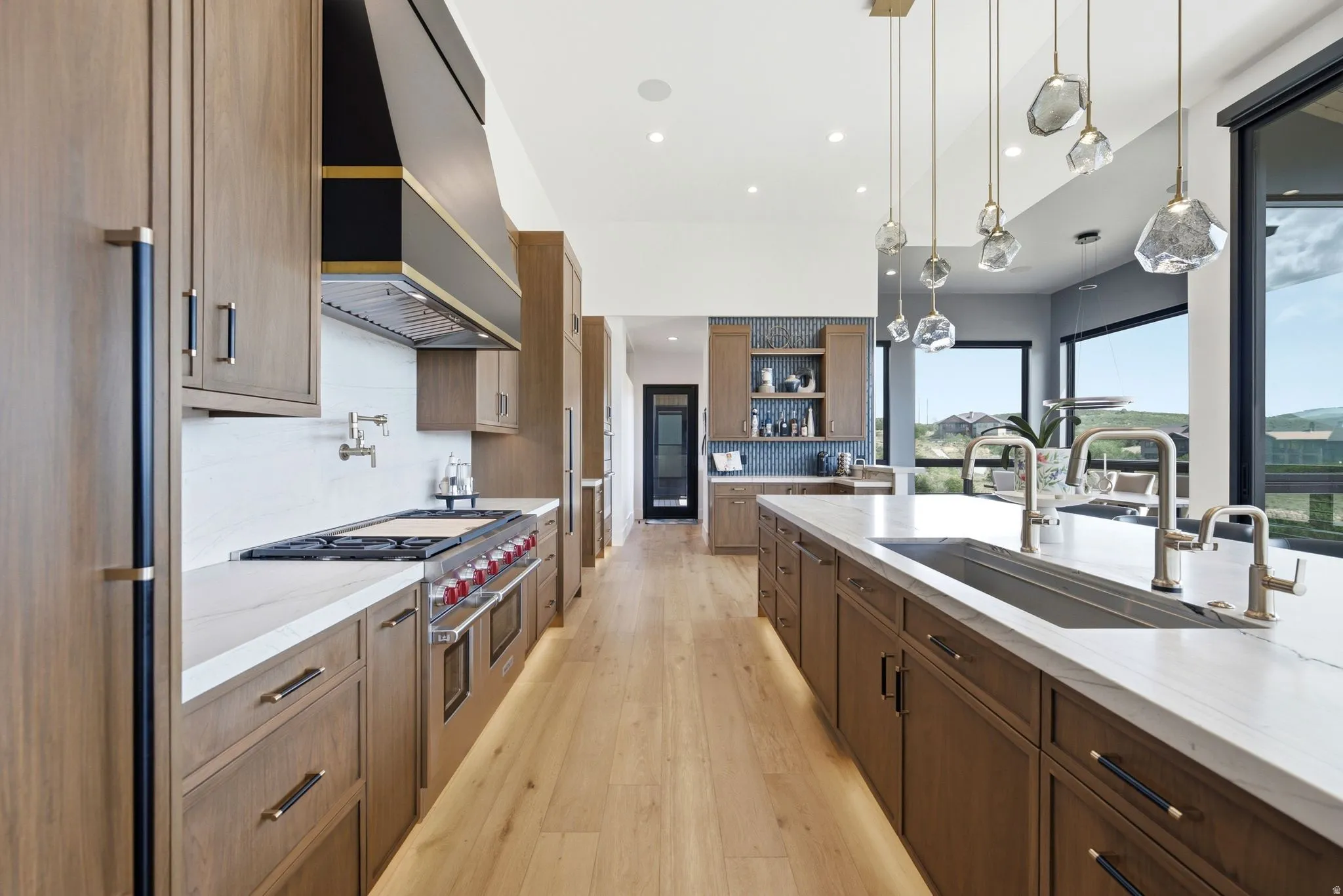 Gourmet kitchen featuring wood-finish cabinetry, a large center island with an undermount sink, stainless steel appliances, and a wall-mounted pot filler