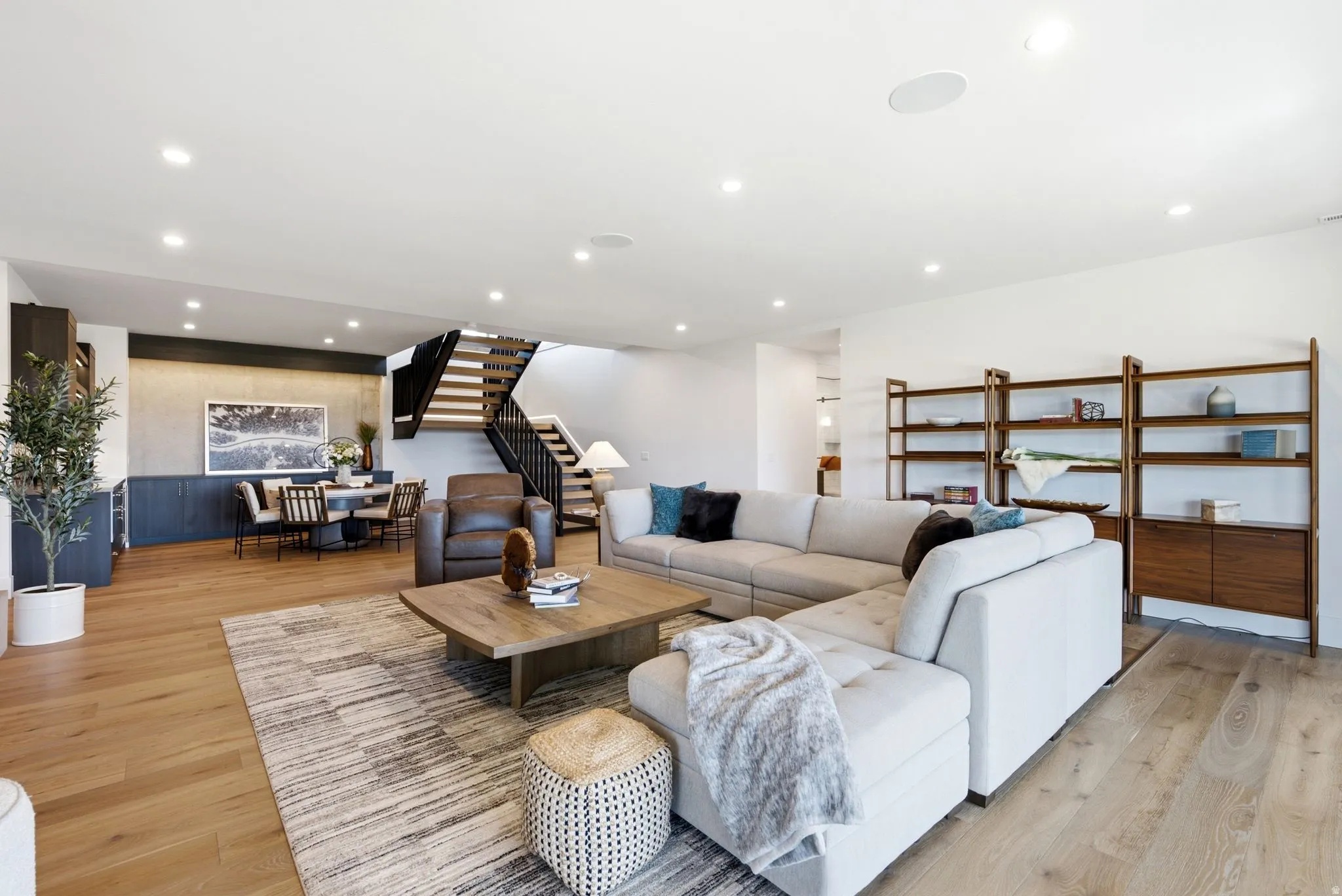 Recessed lighting throughout, wood-finish flooring, open-tread staircase with black railing, built-in shelving, and built-in cabinetry
