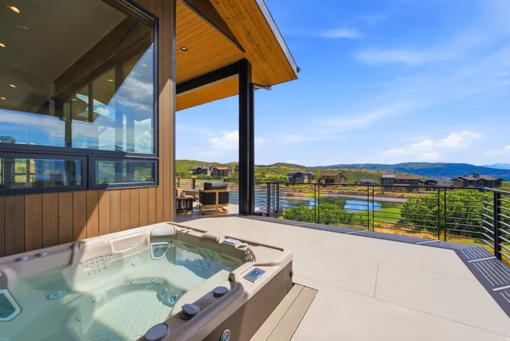Expansive outdoor deck featuring an integrated hot tub, a contemporary cable railing system, a wood-paneled exterior, and large picture windows