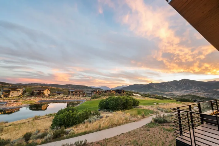 Expansive outdoor balcony with glass and metal railing, overlooking a scenic mountain landscape, a golf course, and a reflective pond