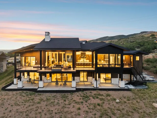 Modern architectural design featuring expansive glass panels, multiple outdoor living spaces, a two-story deck, and a prominent stone-clad chimney