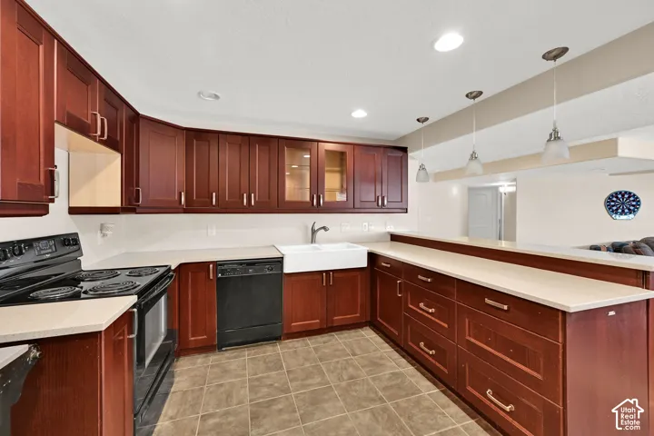 Kitchen featuring wood-finish cabinetry, light-toned countertops, a white apron sink, and pendant lighting