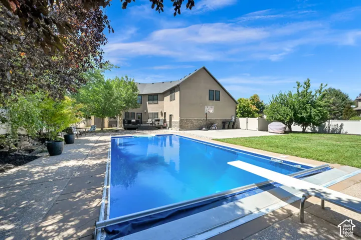 In-ground swimming pool with diving board, concrete patio surround, manicured lawn, and mature landscaping
