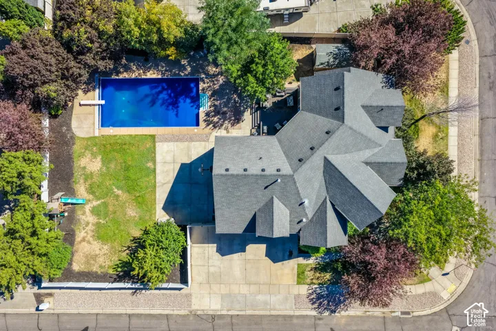 Expansive lot featuring a large in-ground swimming pool with concrete surround, a multi-gabled roofline, mature trees, and a concrete driveway
