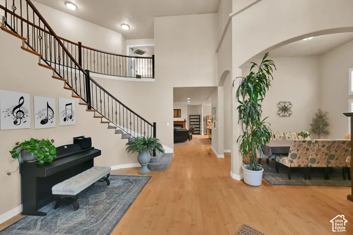 Two-story foyer with wood flooring, a grand staircase with wrought iron balusters, and an arched entry to an additional living space
