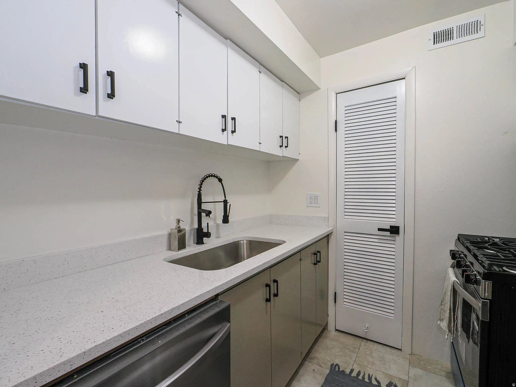 White upper cabinetry with matte black hardware, light-toned countertop, stainless steel undermount sink with a matte black gooseneck faucet, and a stainless steel dishwasher