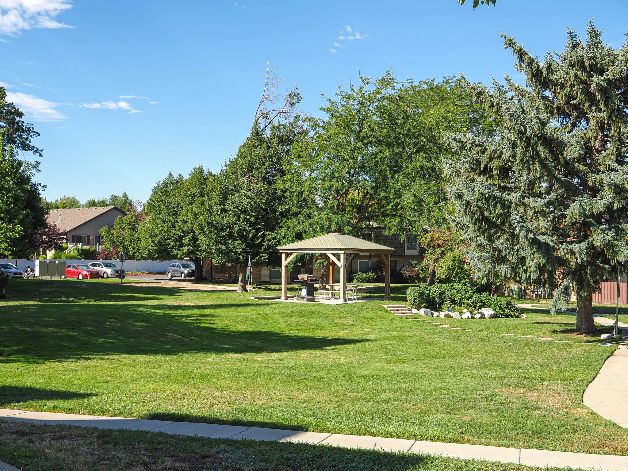Expansive green space featuring a central gazebo, mature trees, landscaped shrubbery, and paved walkways
