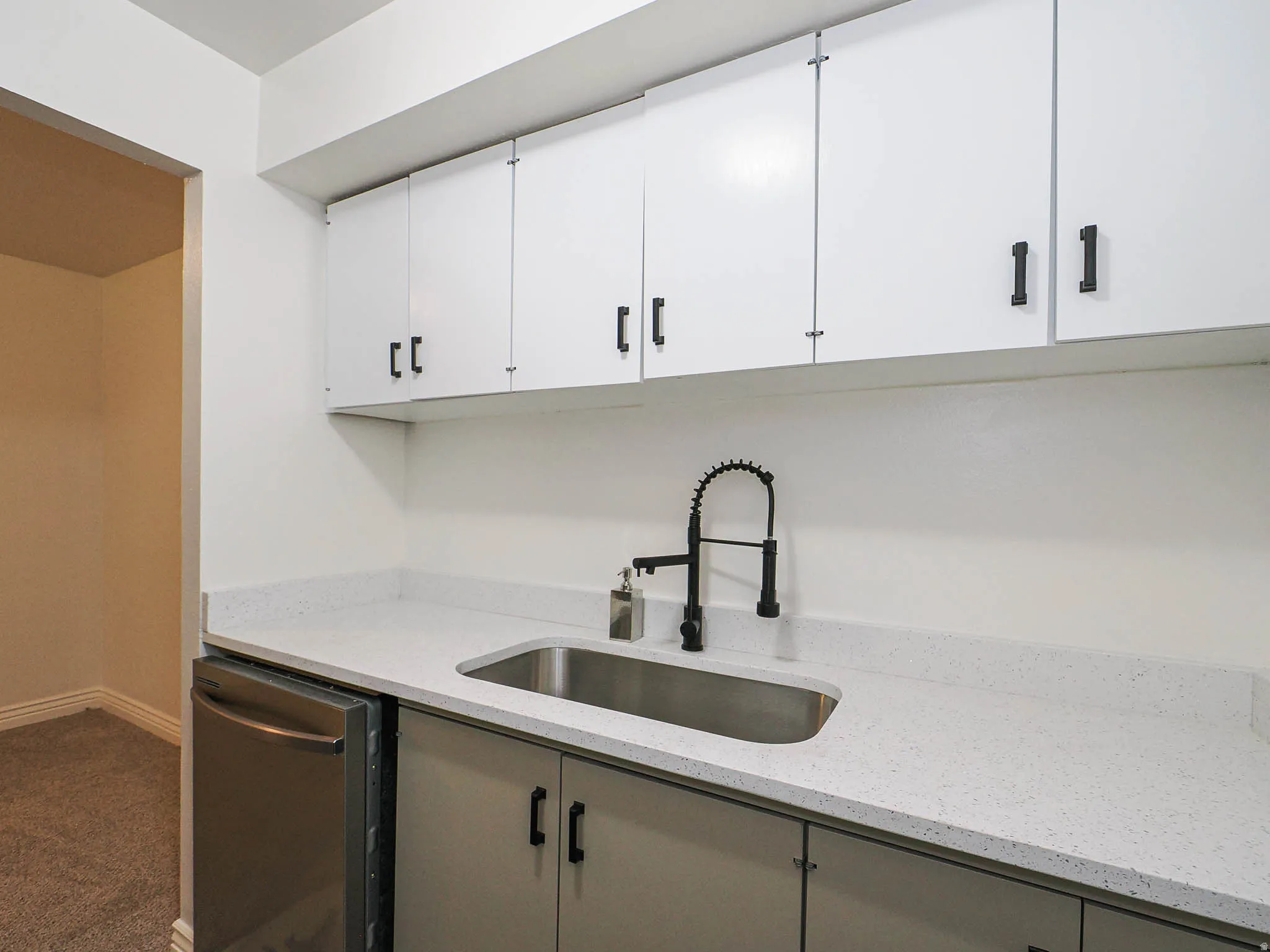Modern kitchenette featuring white cabinetry with matte black hardware, a stainless steel undermount sink, black gooseneck faucet with pull-down spray, quartz countertop, and stainless steel appliances including a dishwasher