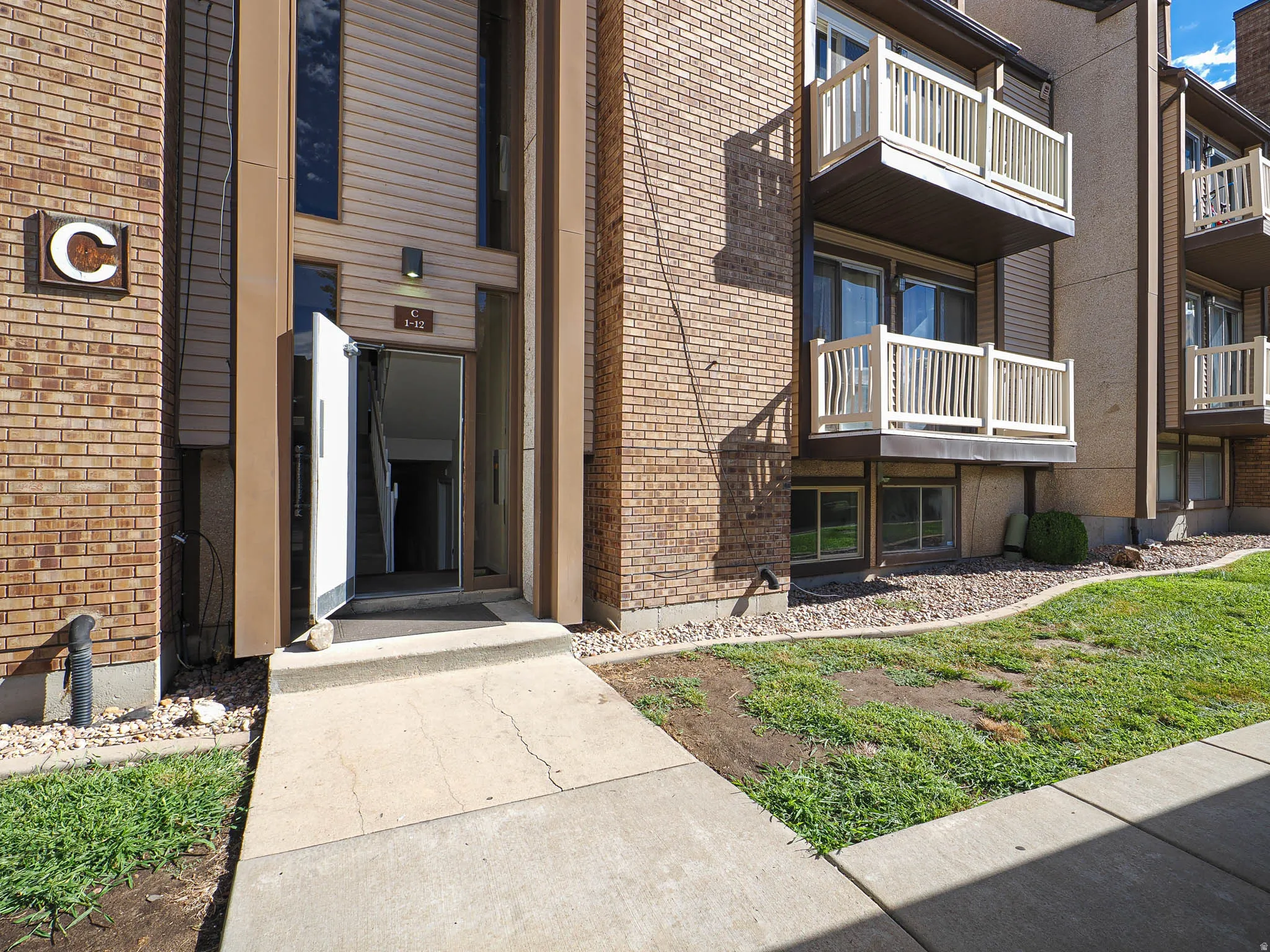 Brick exterior with multiple balconies, ground-level windows, and a paved walkway leading to the entrance