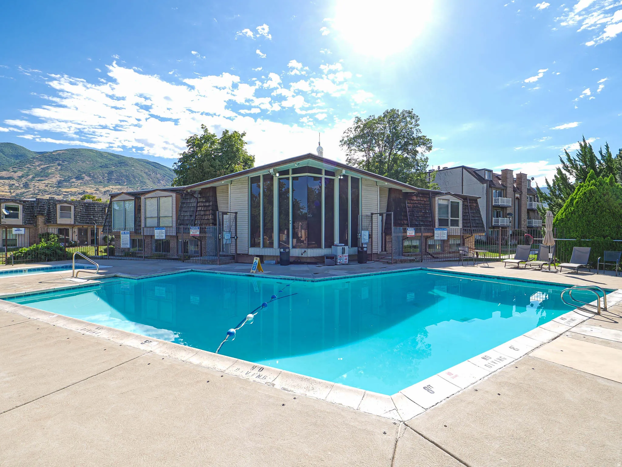 Outdoor swimming pool with concrete surround, adjacent to a building featuring large windows and mountain scenery