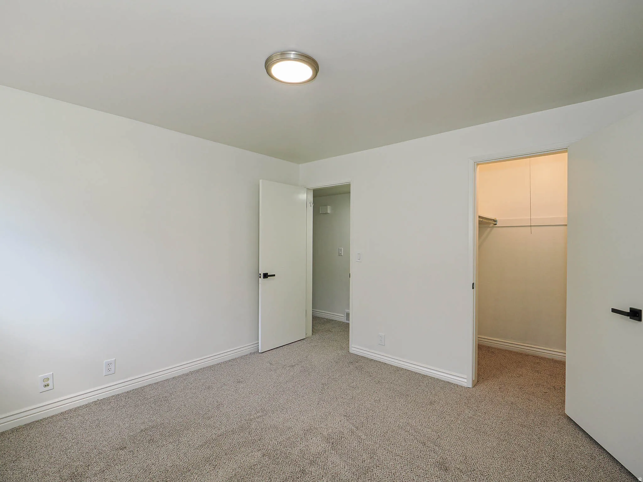 Neutral-toned carpeting, white walls, and a flush-mount ceiling light fixture