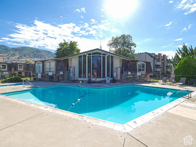 Outdoor swimming pool with concrete surround, adjacent to a building featuring large windows and mountain scenery