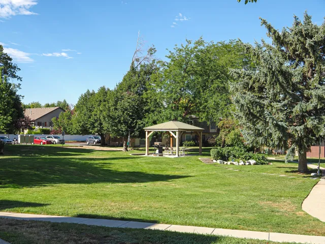 Expansive green space featuring a central gazebo, mature trees, landscaped shrubbery, and paved walkways