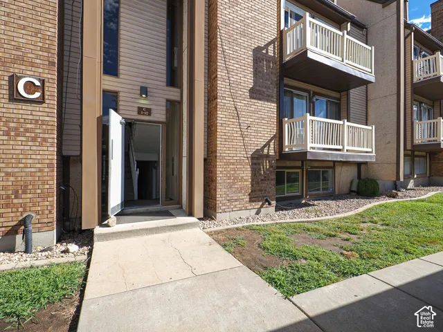 Brick exterior with multiple balconies, ground-level windows, and a paved walkway leading to the entrance