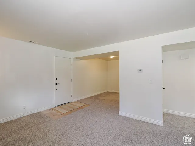 Neutral-toned carpeting, white walls, and a white door with black hardware