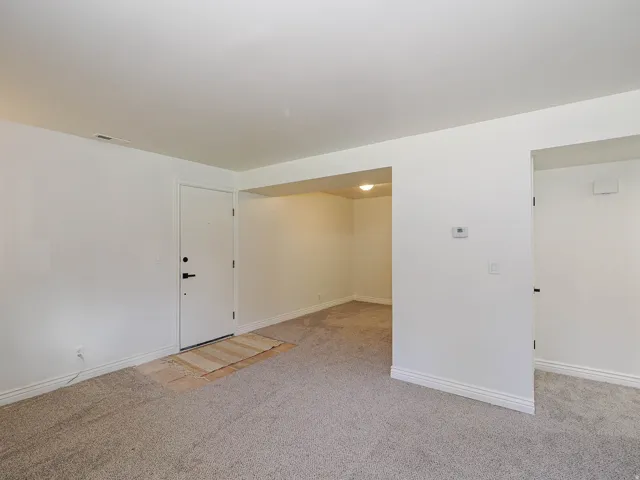 Neutral-toned carpeting, white walls, and a white door with black hardware