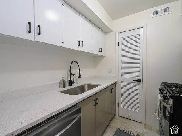 White upper cabinetry with matte black hardware, light-toned countertop, stainless steel undermount sink with a matte black gooseneck faucet, and a stainless steel dishwasher