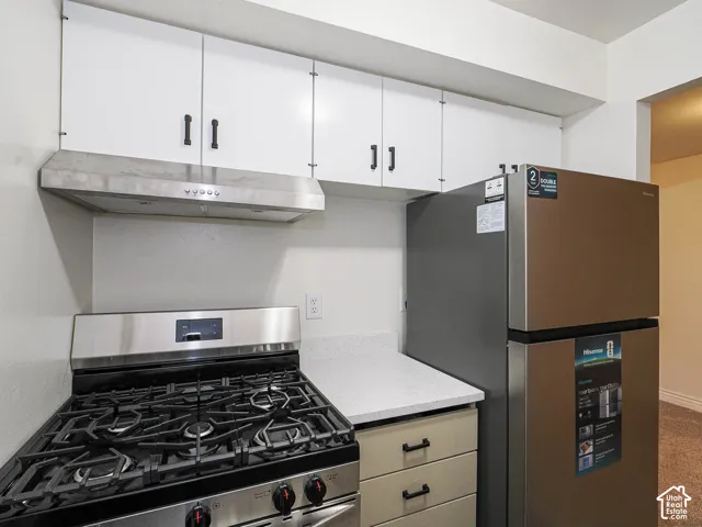 White upper cabinetry, stainless steel range hood, and a gas range